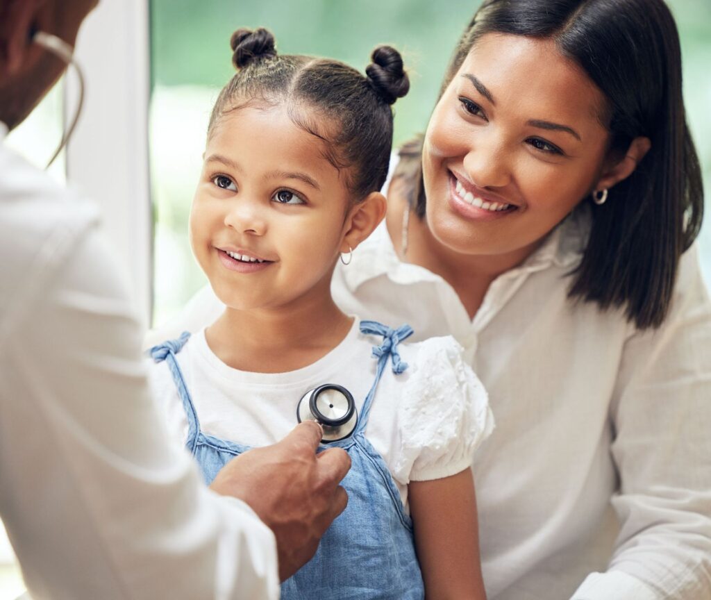 Smiling young girl having her heart checked with a stethoscope while her mother sits beside her