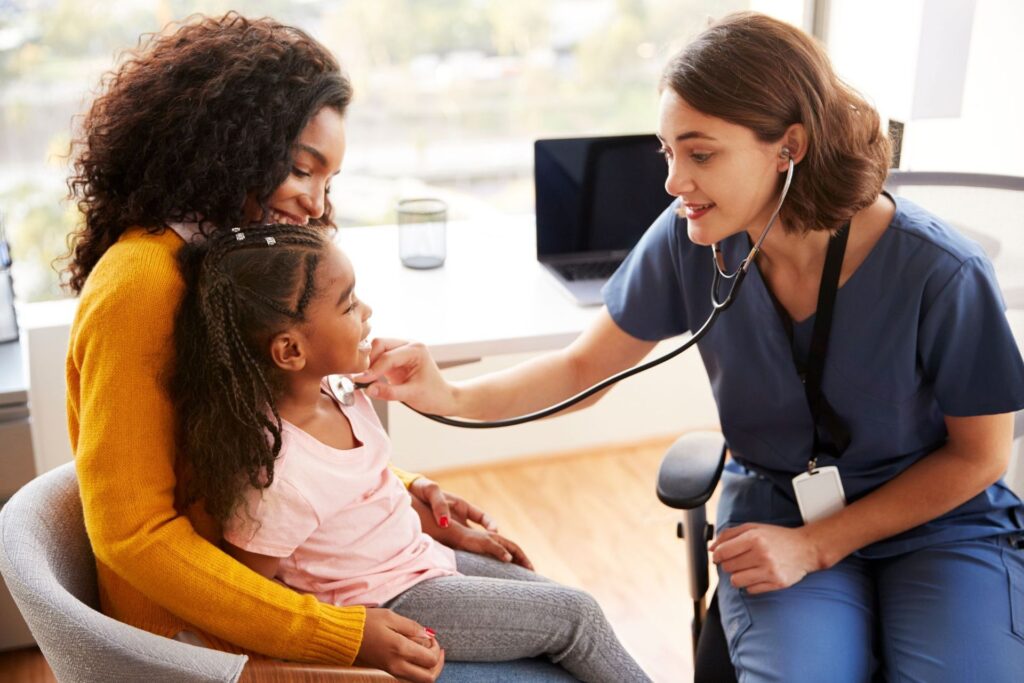 Pediatric nurse listening to a young girl's heart with a stethoscope as her mother holds her