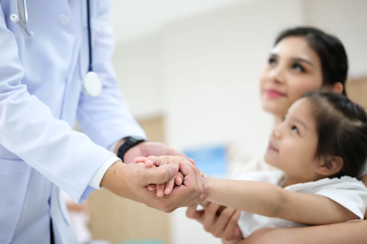 Pediatric provider gently holding a young girl’s hand while she sits in her mother’s lap