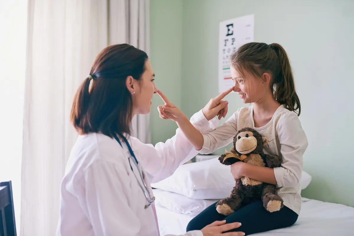 Playful pediatrician and young girl holding a stuffed monkey touching noses during a checkup