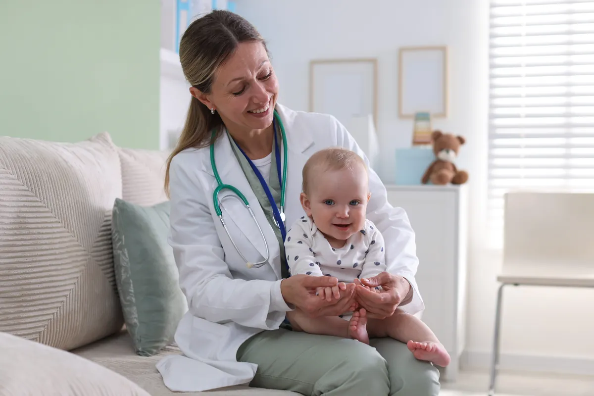 Smiling pediatrician holding a happy baby on her lap in a bright exam room