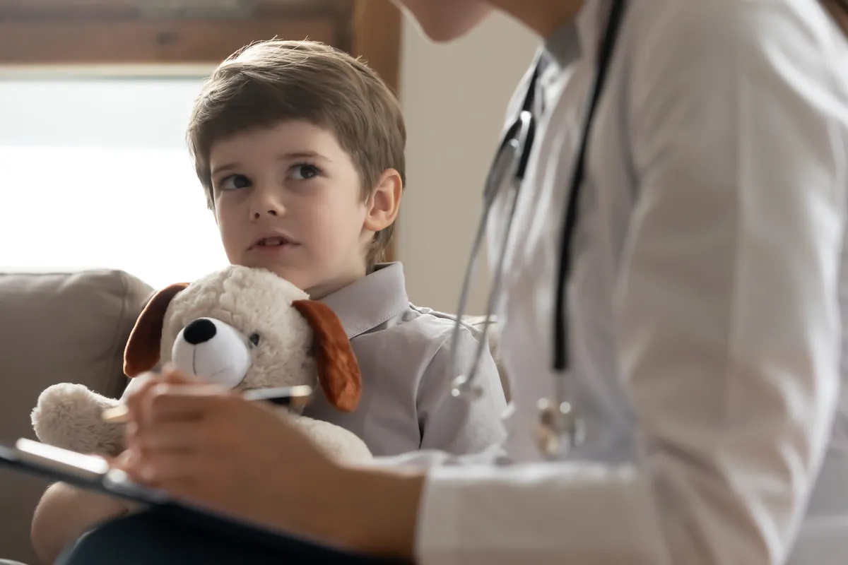 Young boy holding a stuffed puppy and listening as his doctor takes notes